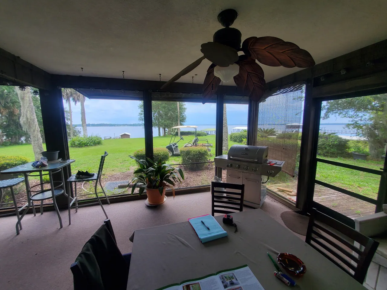 Furnished screened room with dark framing, a ceiling fan and waterfront views.